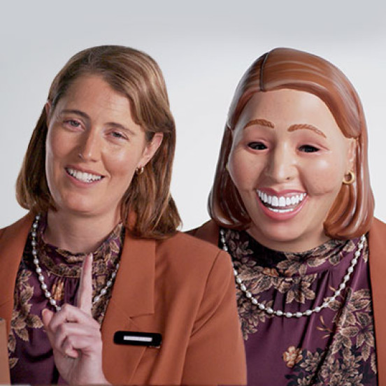 Photo of a woman in a suit with another woman next to her that is dressed the same but wearing a mask