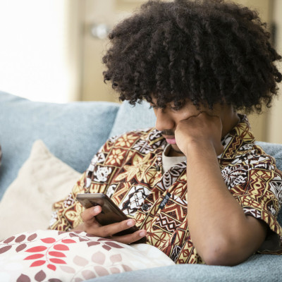 Young man on couch with Pacific patterned shirt on looking at phone