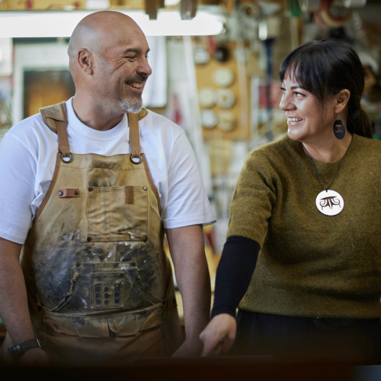 Photo of a man and a woman looking at each other and smiling, with a workshop in the background