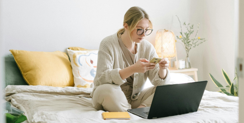 Woman sitting on her bed with a laptop and phone